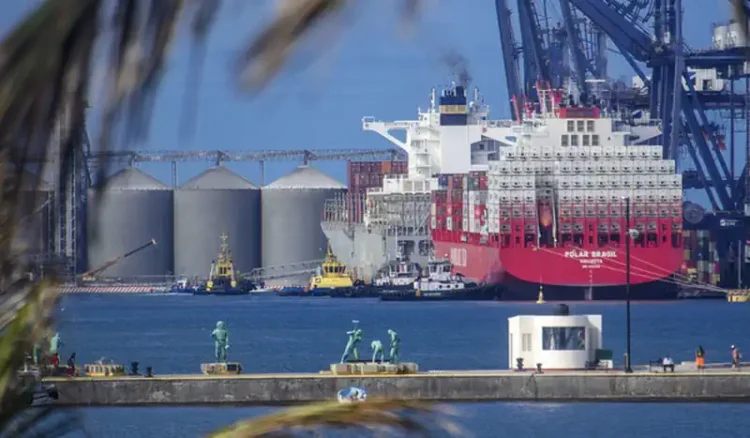 Grúa portuaria y buque de carga en el puerto de Manzanillo, Michoacán, con silos y barcos en el fondo.