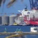 Grúa portuaria y buque de carga en el puerto de Manzanillo, Michoacán, con silos y barcos en el fondo.
