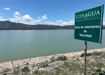 Represa en Michoacán con señal de zona de reductores de velocidad y paisaje montañoso al fondo.