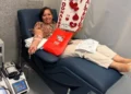 Mujer dona sangre en hospital, participando en campaña solidaria con cartel de "Soy altruista" y corazones rojos.
