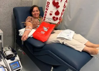 Mujer dona sangre en hospital, participando en campaña solidaria con cartel de "Soy altruista" y corazones rojos.