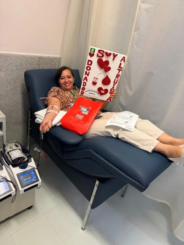 Mujer dona sangre en hospital, participando en campaña solidaria con cartel de "Soy altruista" y corazones rojos.
