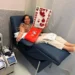 Mujer dona sangre en hospital, participando en campaña solidaria con cartel de "Soy altruista" y corazones rojos.