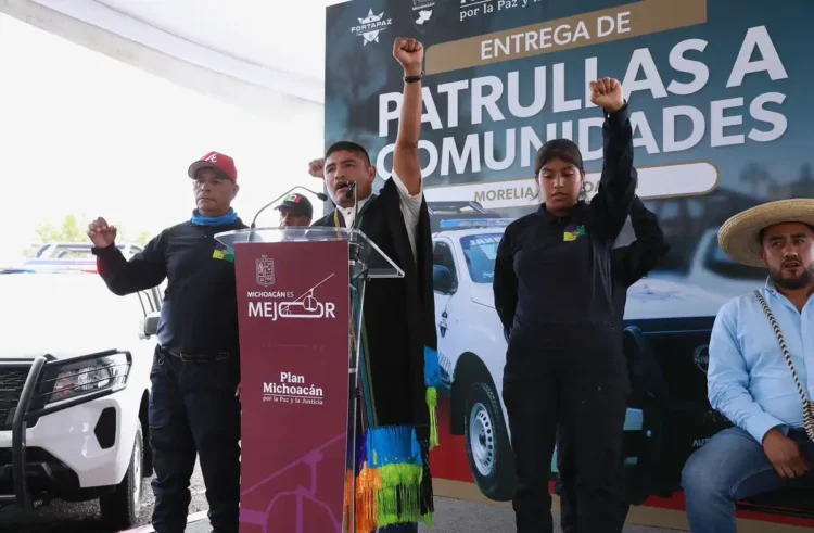 Hombres y mujeres levantan el puño en señal de unidad durante evento de entrega de patrullas.