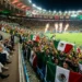 Aficionados mexicanos celebran con banderas en estadio durante partido internacional.