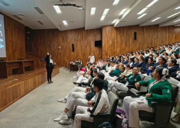 Grupo de estudiantes en uniforme de artes marciales asistiendo a una clase en un auditorio con madera en las paredes.