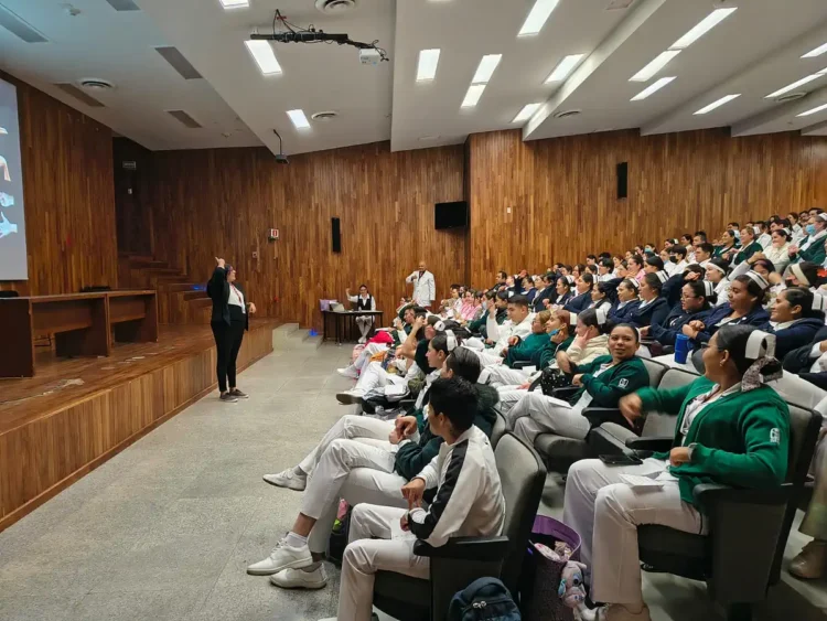 Grupo de estudiantes en uniforme de artes marciales asistiendo a una clase en un auditorio con madera en las paredes.