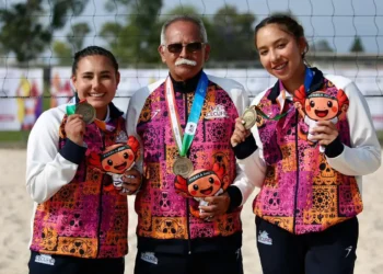 Dos jóvenes deportistas mexicanas y un entrenador posan con medallas en torneo de voleibol de playa en Jalisco.