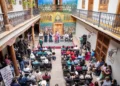 Reunión de comerciantes y autoridades en un patio colonial con murales coloridos en Pátzcuaro.