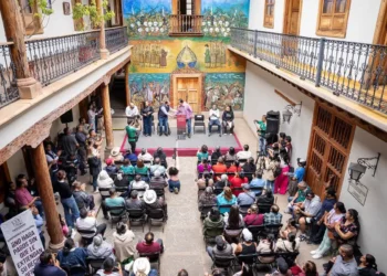Reunión de comerciantes y autoridades en un patio colonial con murales coloridos en Pátzcuaro.
