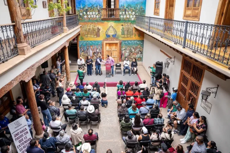 Reunión de comerciantes y autoridades en un patio colonial con murales coloridos en Pátzcuaro.