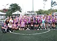 Equipo femenino de fútbol en uniforme morado y blanco en un campo de césped artificial.