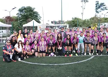 Equipo femenino de fútbol en uniforme morado y blanco en un campo de césped artificial.