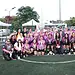 Equipo femenino de fútbol en uniforme morado y blanco en un campo de césped artificial.