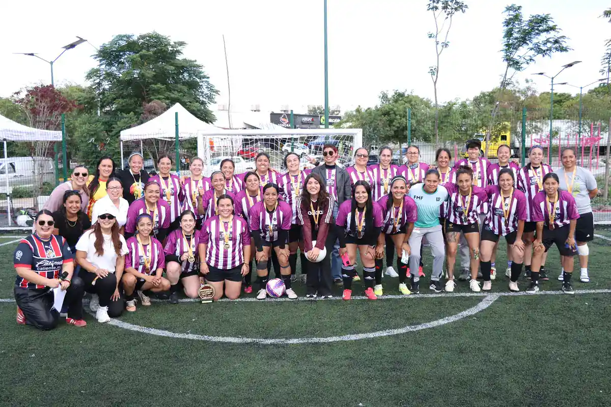 Equipo femenino de fútbol en uniforme morado y blanco en un campo de césped artificial.