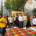 Grupo de personas en reunión política con bandera del PRD en fondo de muro de ladrillos y plantas.