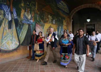 Personas caminando frente a mural colorido en evento cultural en Michoacán.