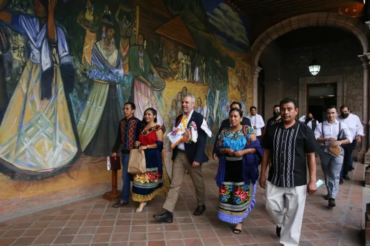 Personas caminando frente a mural colorido en evento cultural en Michoacán.
