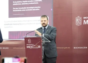 Hombre en traje oscuro hablando en conferencia en un escenario con fondo rojo y logotipo del gobierno de Michoacán.