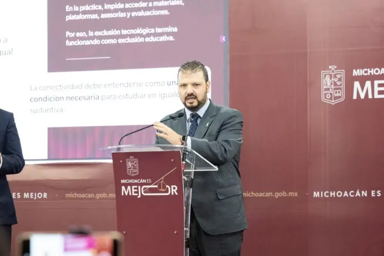 Hombre en traje oscuro hablando en conferencia en un escenario con fondo rojo y logotipo del gobierno de Michoacán.