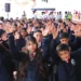 Niños y niñas en uniforme escolar levantando las manos en una actividad en un evento escolar.