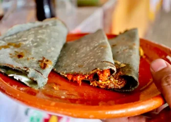 Tacos de tinga en tortilla de maíz en un plato de barro, con fondo difuso de puestos callejeros en Morelia.