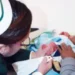 Recien nacido en incubadora con personal médico y familiares en fondo blanco.