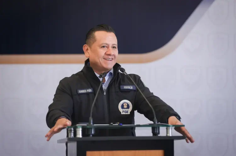 Torres Piña en conferencia de prensa, vestido con uniforme de fiscalía, sonriendo mientras habla frente a micrófonos.