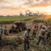Trabajadores cosechan caña de azúcar en un campo al atardecer, con maquinaria agrícola y un cielo nublado en el fondo.