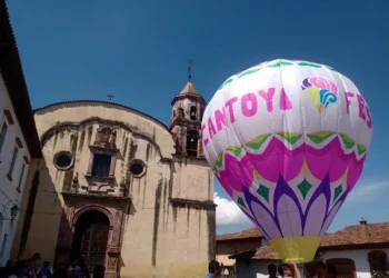 Globo aerostático con colores vibrantes y logotipo del Cantoya Fest en Pátzcuaro, con iglesia antigua de fondo y cielo despej.