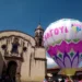 Globo aerostático con colores vibrantes y logotipo del Cantoya Fest en Pátzcuaro, con iglesia antigua de fondo y cielo despej.