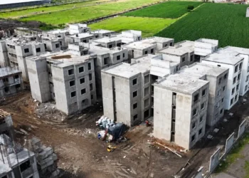 Edificios en construcción en un área rural de Michoacán, con campos verdes en el fondo y maquinaria en el sitio.