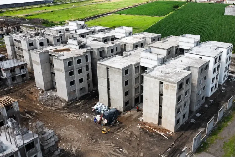 Edificios en construcción en un área rural de Michoacán, con campos verdes en el fondo y maquinaria en el sitio.