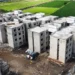 Edificios en construcción en un área rural de Michoacán, con campos verdes en el fondo y maquinaria en el sitio.