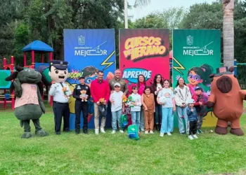 Niños y adultos disfrutan actividades en parque con personajes de caricaturas y banners promocionales de cursos de verano.