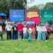 Niños y adultos disfrutan actividades en parque con personajes de caricaturas y banners promocionales de cursos de verano.