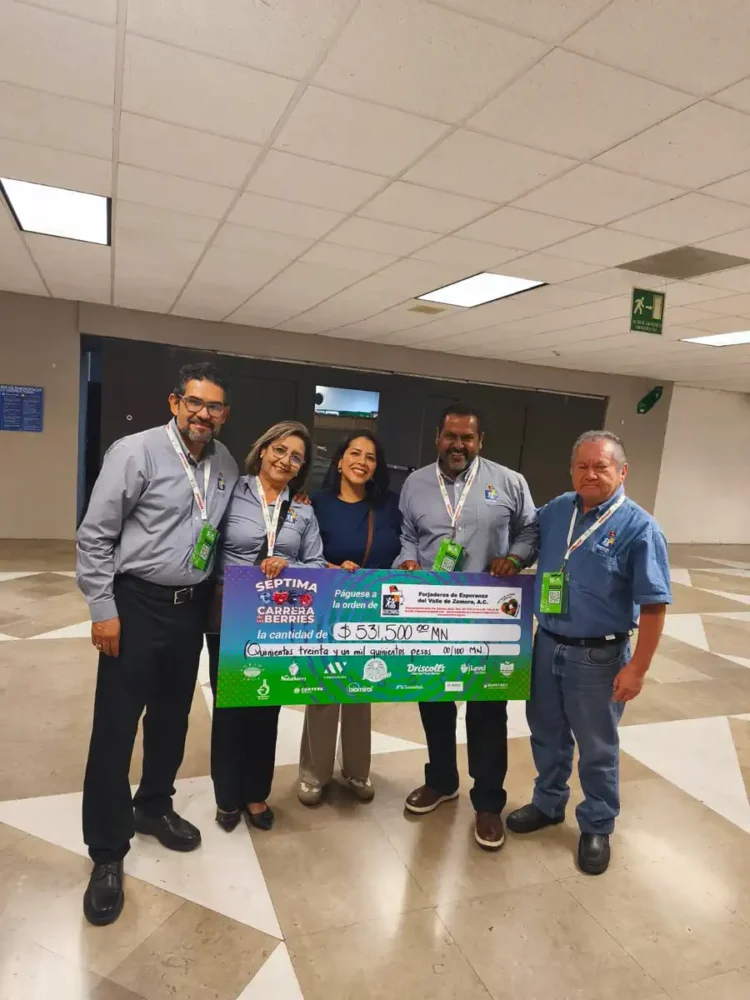 Grupo de cinco personas sosteniendo un cheque grande en un espacio interior, celebrando donativo récord de Aneberries.
