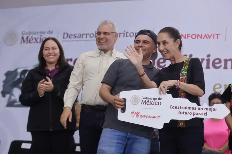 Cuatro personas en un evento oficial con fondo de logotipos del gobierno y patrocinadores, sonriendo y sosteniendo un cartel.