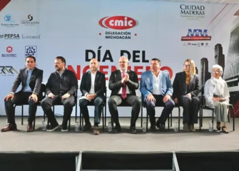 Funcionarios y expertos en evento oficial en Michoacán, sentados en una mesa con fondo de logotipos y cartel.
