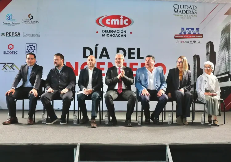 Funcionarios y expertos en evento oficial en Michoacán, sentados en una mesa con fondo de logotipos y cartel.