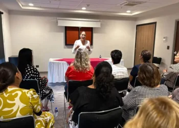 Mujer dando conferencia en taller de tanatología en Zamora, con asistentes atentos en sala moderna.