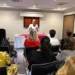 Mujer dando conferencia en taller de tanatología en Zamora, con asistentes atentos en sala moderna.