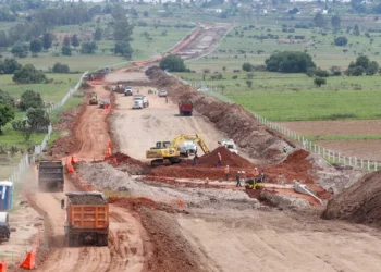 Maquinaria y trabajadores en construcción de libramiento en Michoacán, con maquinaria pesada y tierra en movimiento.