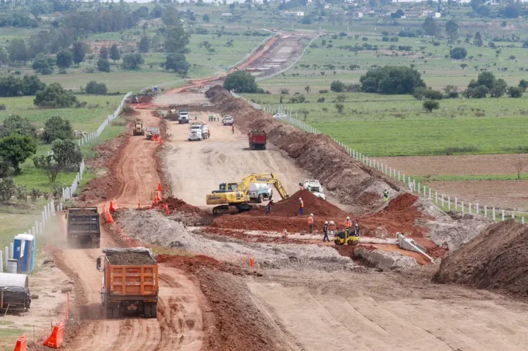 Maquinaria y trabajadores en construcción de libramiento en Michoacán, con maquinaria pesada y tierra en movimiento.