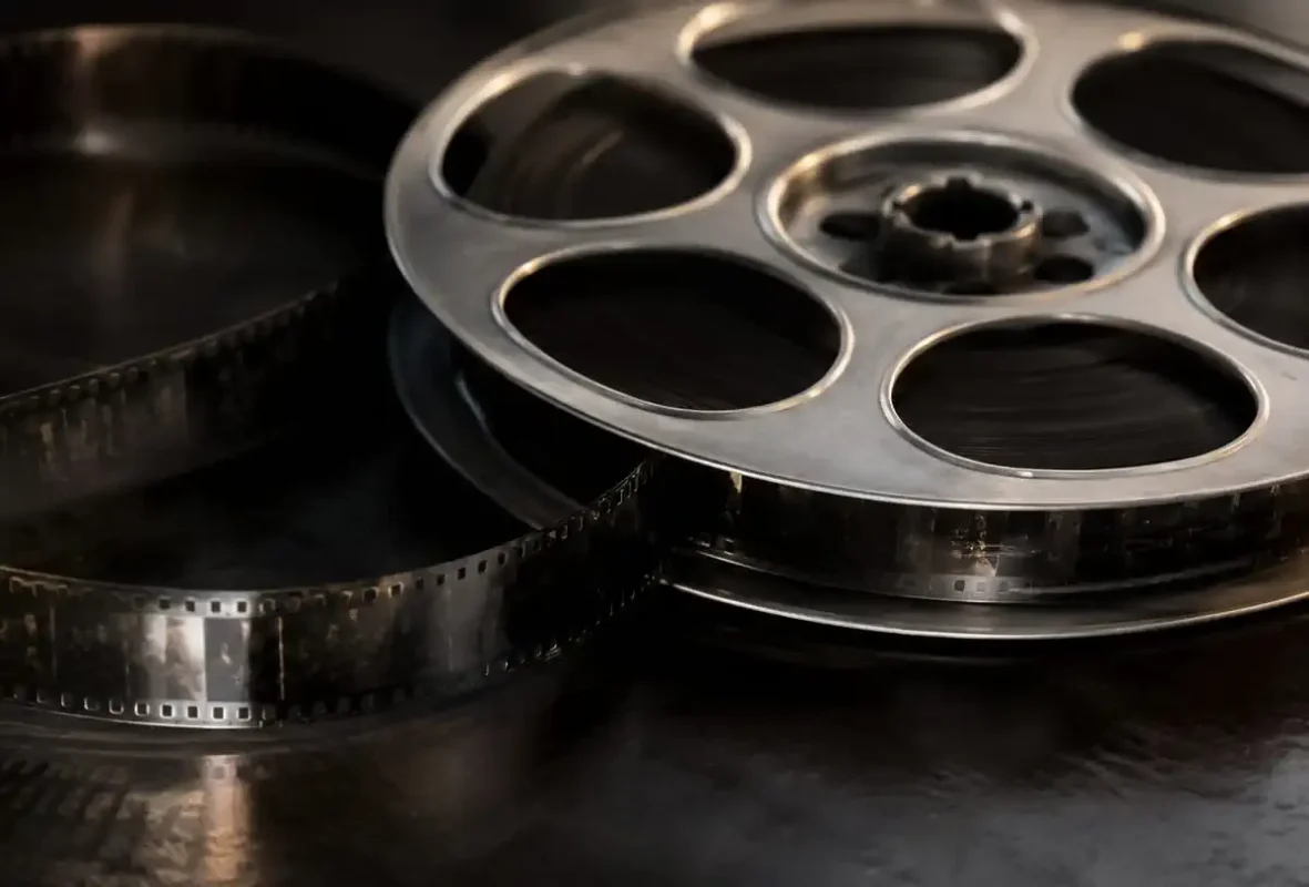 Rollo de película de cine en primer plano, con detalles metálicos y perforaciones, sobre fondo oscuro.