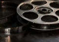 Rollo de película de cine en primer plano, con detalles metálicos y perforaciones, sobre fondo oscuro.