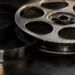 Rollo de película de cine en primer plano, con detalles metálicos y perforaciones, sobre fondo oscuro.