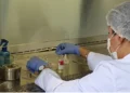 Técnico en laboratorio con bata, guantes y mascarilla manipulando muestras en un entorno controlado.