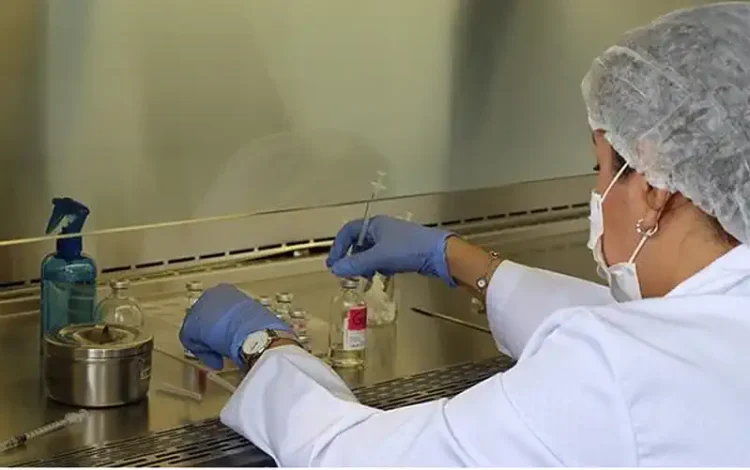 Técnico en laboratorio con bata, guantes y mascarilla manipulando muestras en un entorno controlado.
