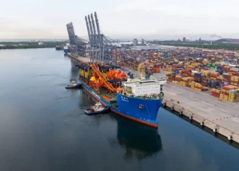 Puerto de carga en Michoacán con contenedores y grúas en el muelle, barcos y almacenes de mercancías en el fondo.